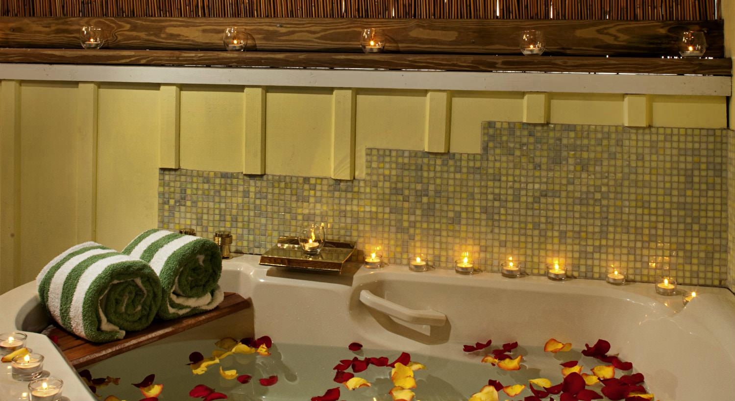 Large jacuzzi tub with red and yellow flower petals in water surrounded by small lit candles for mood lighting