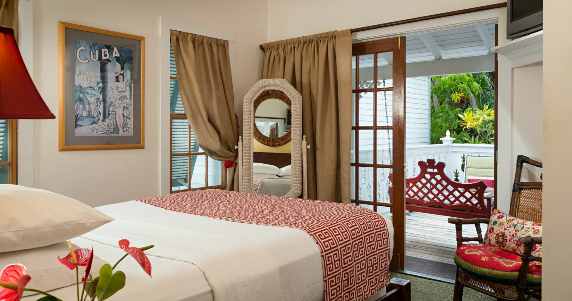 Bedroom with white walls with glass doors leading onto enclosed patio with sitting chair and flat screen tv on shelf