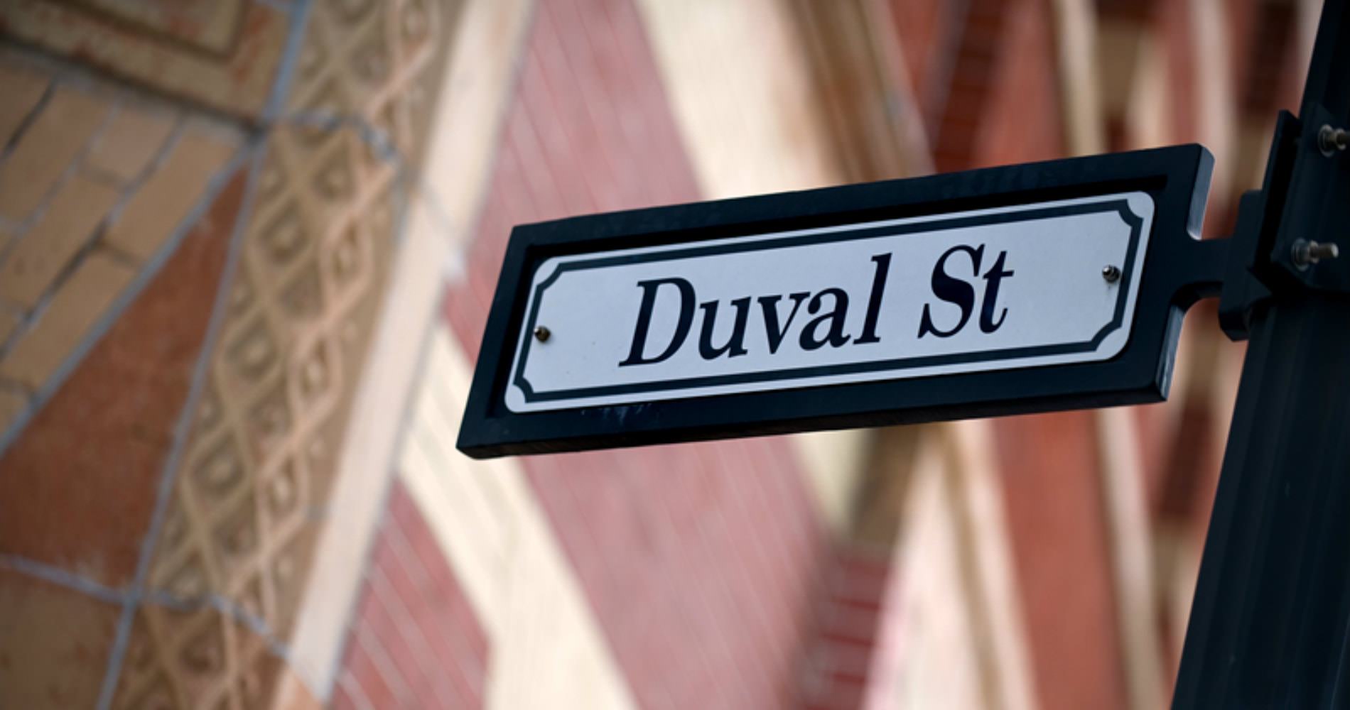 Black and white rectangular street sign Duval street next to brick building