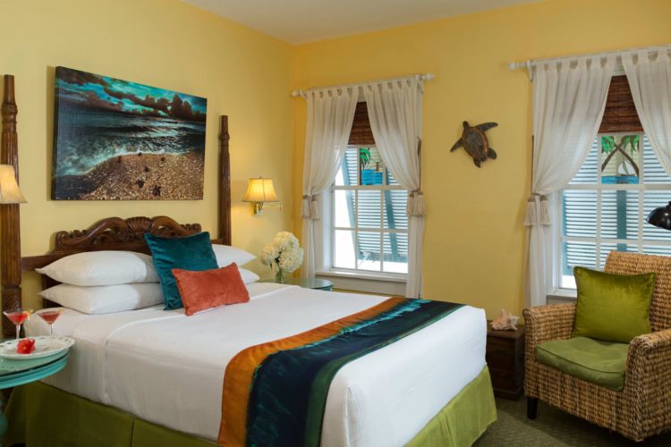 Yellow bedroom with twin bed and turtle decoration on wall with end table with champagne flutes with 2 windows