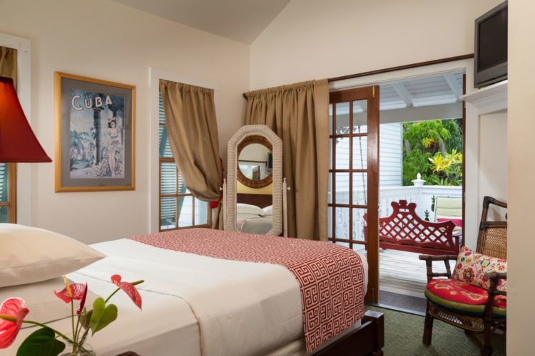 Bedroom with white walls with glass doors leading onto enclosed patio with sitting chair and flat screen tv on shelf