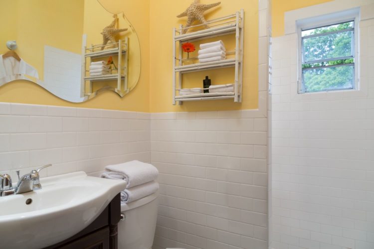 Yellow bathroom with white tile on walls and die cut mirror above sink which is next to toilet