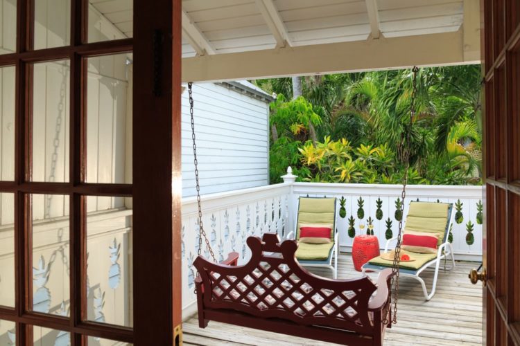 Balcony with lounge chairs with yellow cushions and pillows with hanging porch swing enclosed with white fence