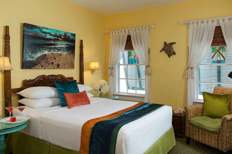 Yellow bedroom with twin bed and turtle decoration on wall with end table with champagne flutes with 2 windows