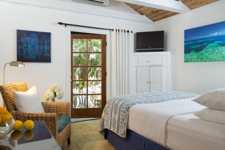 White painted bedroom with door leading to patio with white cabinet in corner with television and cushioned wicker chair