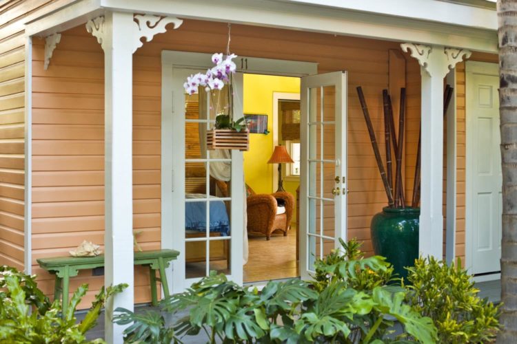 Patio with opened white glass door leading into yellow sitting rom with hanging planter on patio