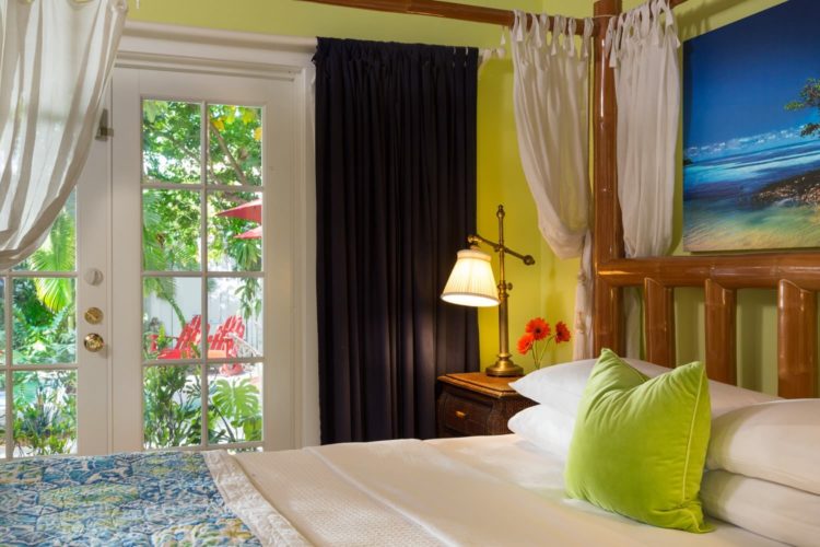 Bright yellow bedroom with 4 poster canopy bed with glass door leading to garden with red wooden chairs