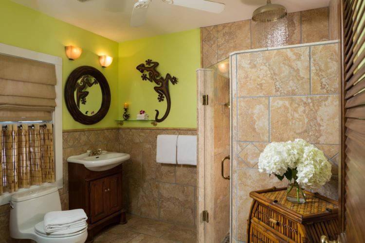 Bright yellow bathroom with gecko figurine on wall with walk in tiled shower with sink with bamboo mirror