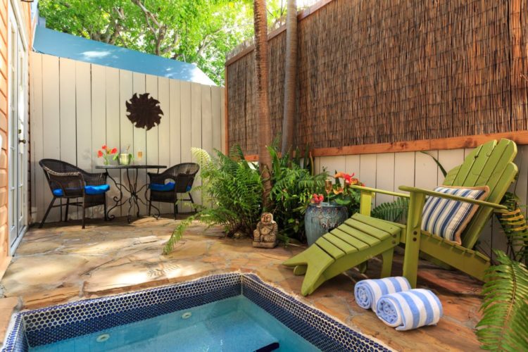 Enclosed patio with hot tub and lime green lounge chair with green and white striped pillow with table in background