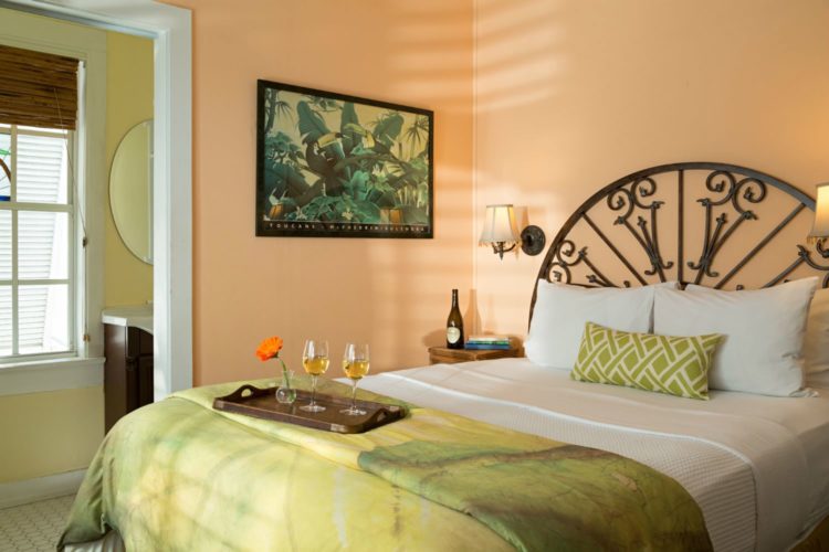 Peach bedroom with iron headboard with green comforter connected to yellow room with sink and oval mirror