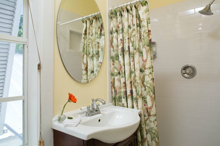 Sink with oval mirror above with walk in shower with white tile with green and tan shower curtain