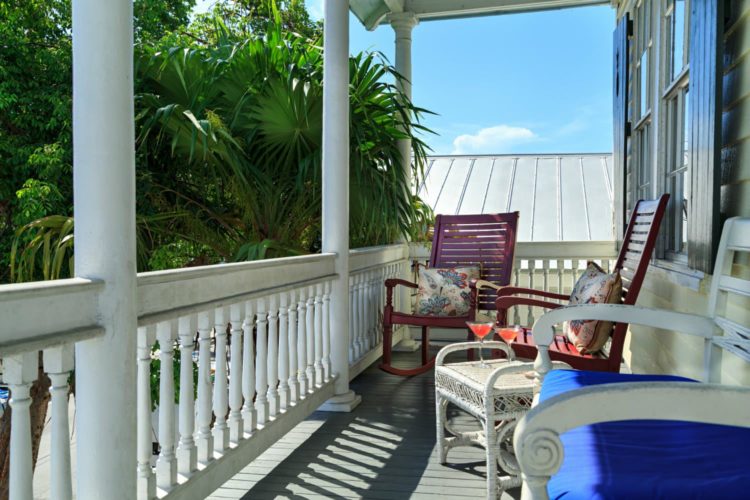 2nd story covered balcony with 2 wood rocking chairs with pillows sitting in front of windows and white cushioned bench