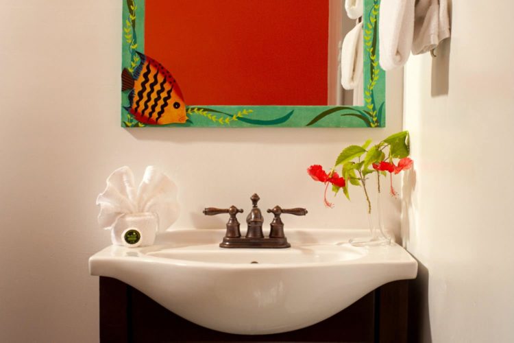 Sink with antique brass fixtures and mirror painted with ocean scene (fish in corner) and towels hanging on wall