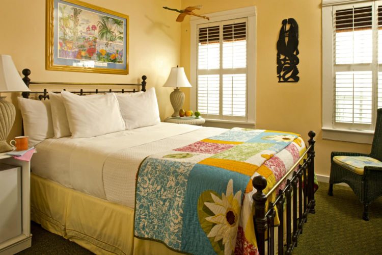 Mustard yellow bedroom with painting above bed and patchwork quilt with iron head and foot boards with 2 windows