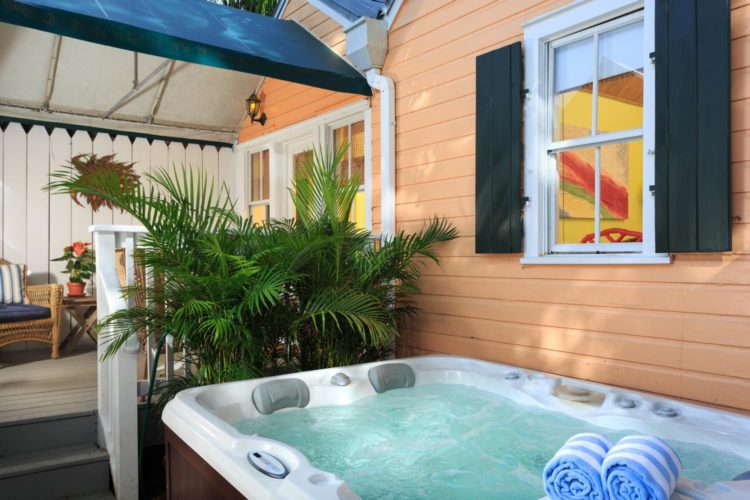 Hot tub with blue and white towels and covered patio with cushioned bamboo chairs next to peach building
