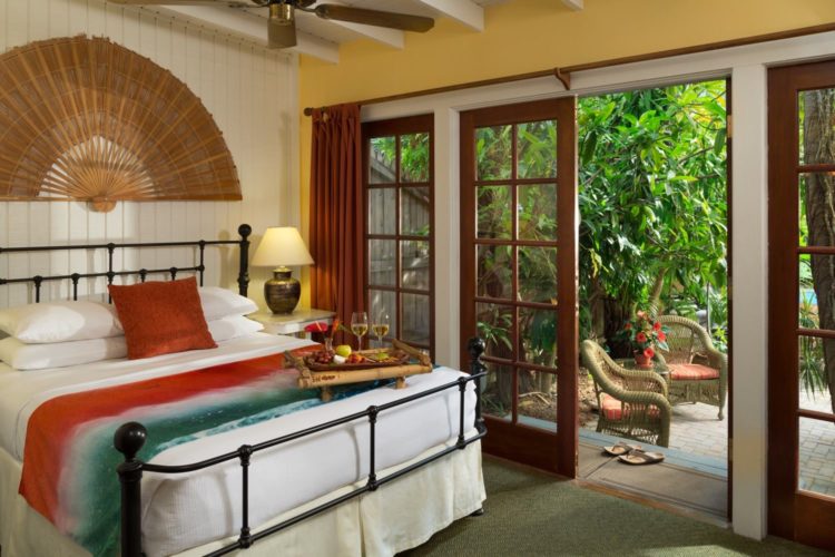 Bedroom with queen bed and wicker fan decoration with ceiling fan and glass doors leading to patio with wicker chairs