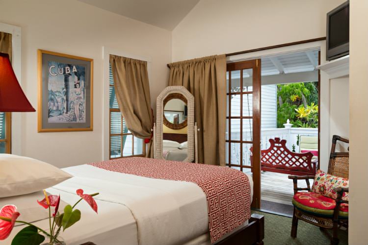 Bedroom with white walls with glass doors leading onto enclosed patio with sitting chair and flat screen tv on shelf