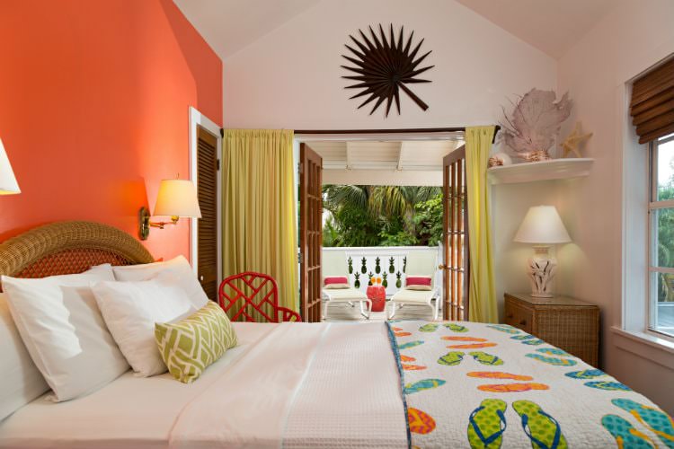 Bed with comforter with flip flops entered onto enclosed patio with cream lounge chairs with seashells on shelf in corner