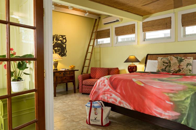 Canary yellow room with loft and king size bed with peach and green bedspread and end table with lamp