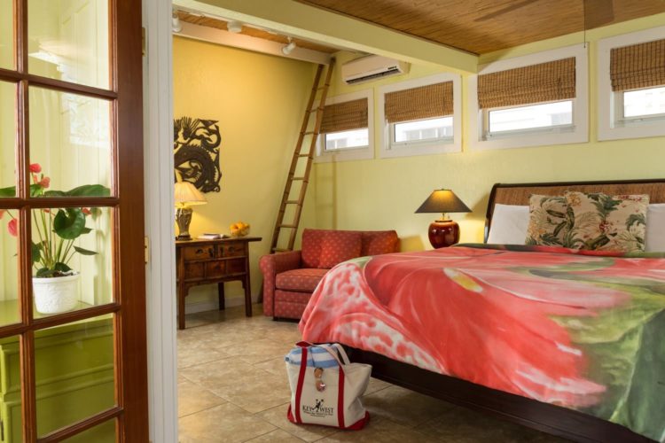 Canary yellow room with loft and king size bed with peach and green bedspread and end table with lamp