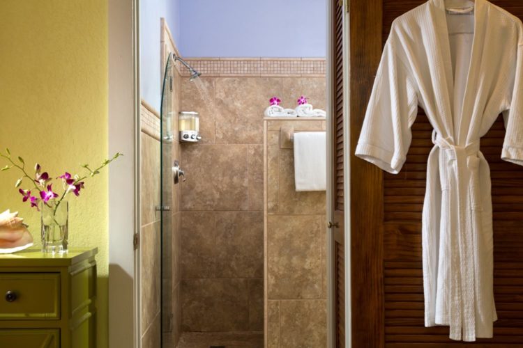 Yellow room with door leading to bathroom with marble tiled shower and white robe hanging on door