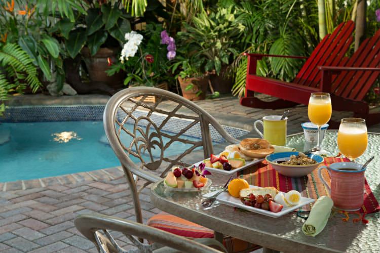 Glass table with breakfast food with red chairs and pool in background