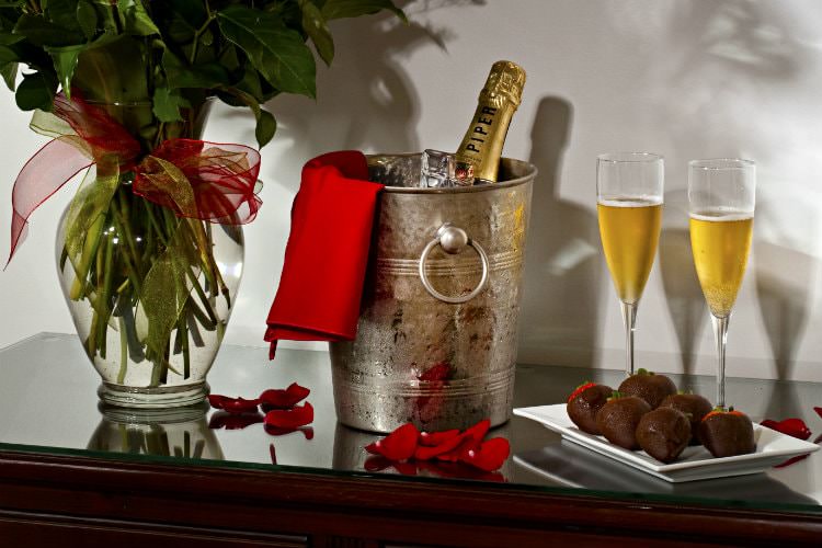 Brown table with champagne glasses and chocolate covered strawberries and metal bucket with champagne bottle