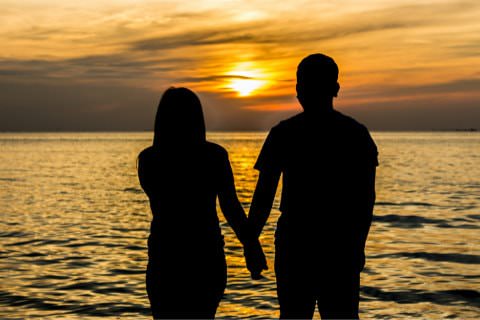 - Man and woman silhouettes holding hands on beach looking at sunset