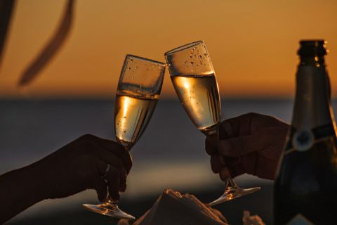 Couple clinking champagne glasses together with sun setting in background