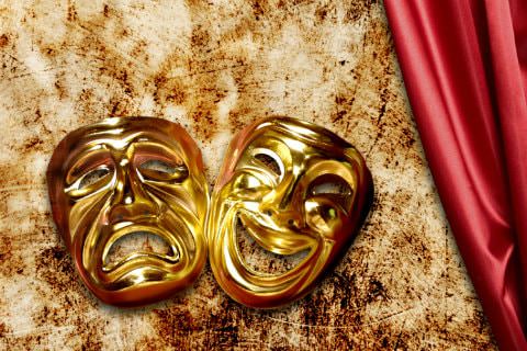 2 shiny gold masks (1 smiling and 1 frowning) on brown and white blanket with red silky material next to it