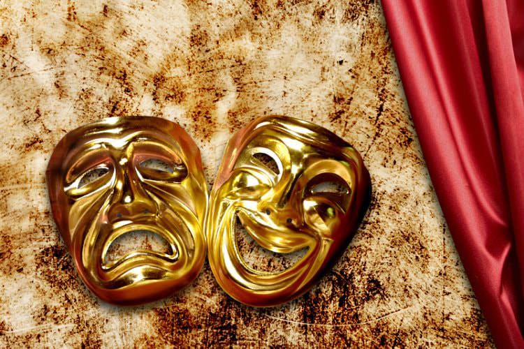 2 shiny gold masks (1 smiling and 1 frowning) on brown and white blanket with red silky material next to it