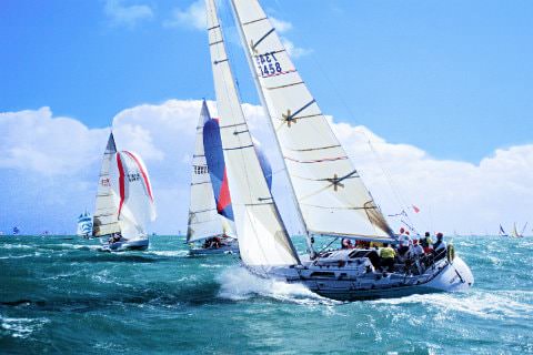 A group of sailboats on the choppy ocean waters with bright blue sky and fluffy clouds in background