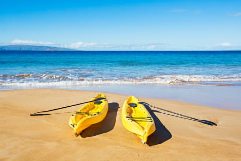 Two yellow plastic kayaks on sandy beach with blue ocean
