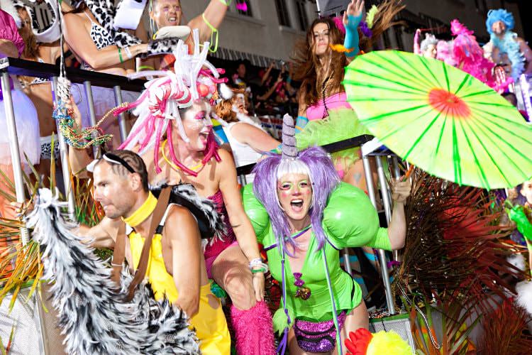 People dressed up in bright costumes with black railing in background dancing at a festive celebration