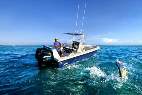 Man fishing on motor boat in middle of ocean with 1 fish on line