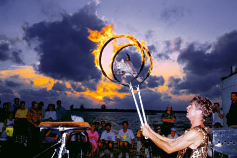 Group of people on beach watching flaming hoop male performer at dusk