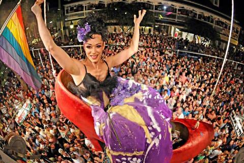 Woman in a giant red shoe suspended from the ceiling over a large crowd of people on new year’s eve