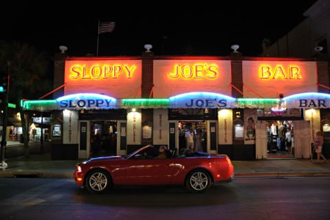 Shiny red convertible on the street in front of Sloppy Joe’s Bar at night