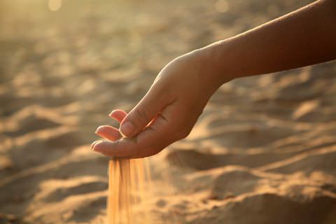 Woman’s arm on a sunny day with sand sifting through bent hand