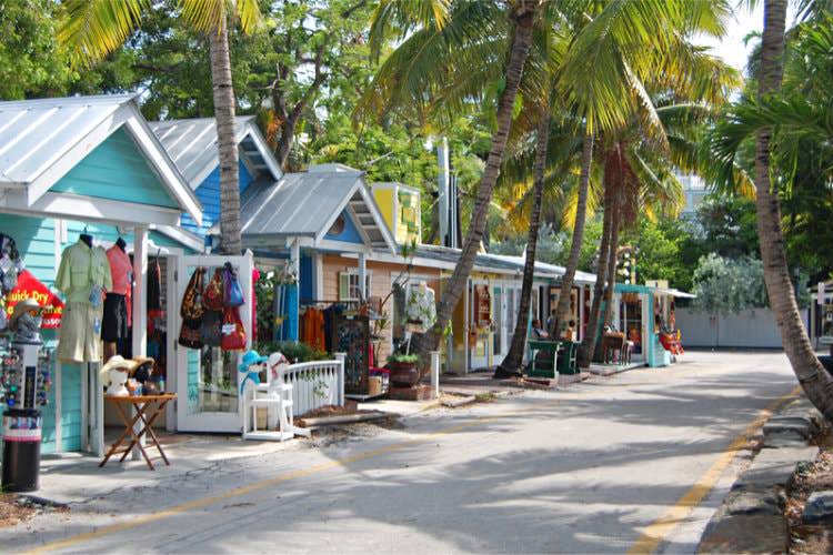 Colorful stores along street surrounded by palm trees with variety of merchandise hanging in front