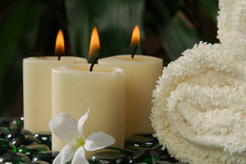 3 burning cream candles next to cream fluffy towels with Lily in front sitting on shiny stones