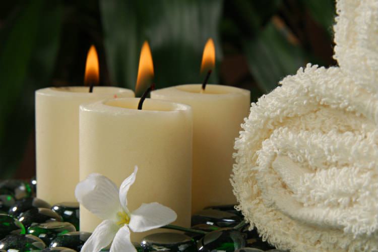 3 burning cream candles next to cream fluffy towels with Lily in front sitting on shiny stones