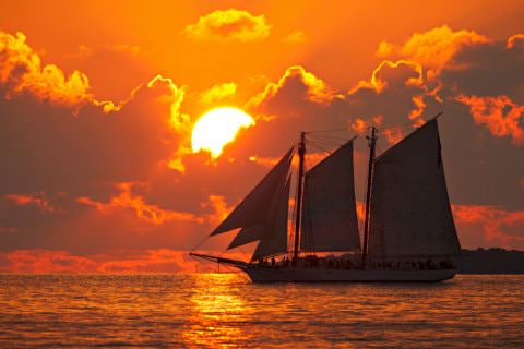 Sailboat on ocean with sun setting in background