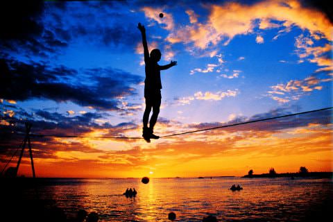 Silhouette figure standing on tightrope over the ocean with sun setting in background