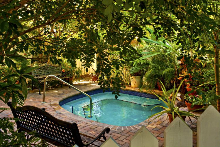 2 metal and wood benches with square pool surrounded by ferns and other plants all enclosed within picket fence