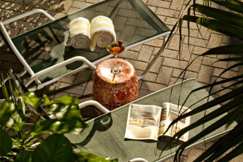 Mesh lounge chairs with yellow and white towels and magazine on chair with table containing champagne flute