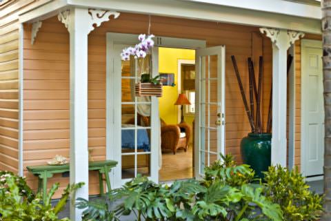 Patio with opened white glass door leading into yellow sitting rom with hanging planter on patio