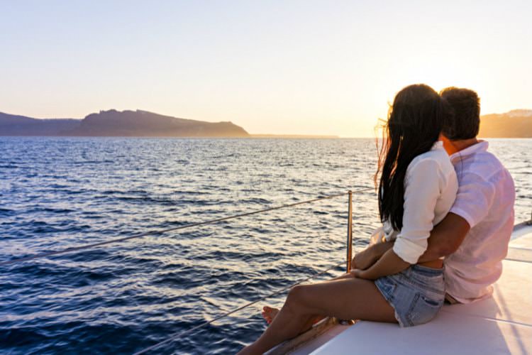 Couple hugging while sitting on pier looking across ocean to the landscape in distance