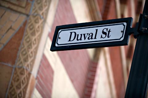 Black and white rectangular street sign Duval street next to brick building