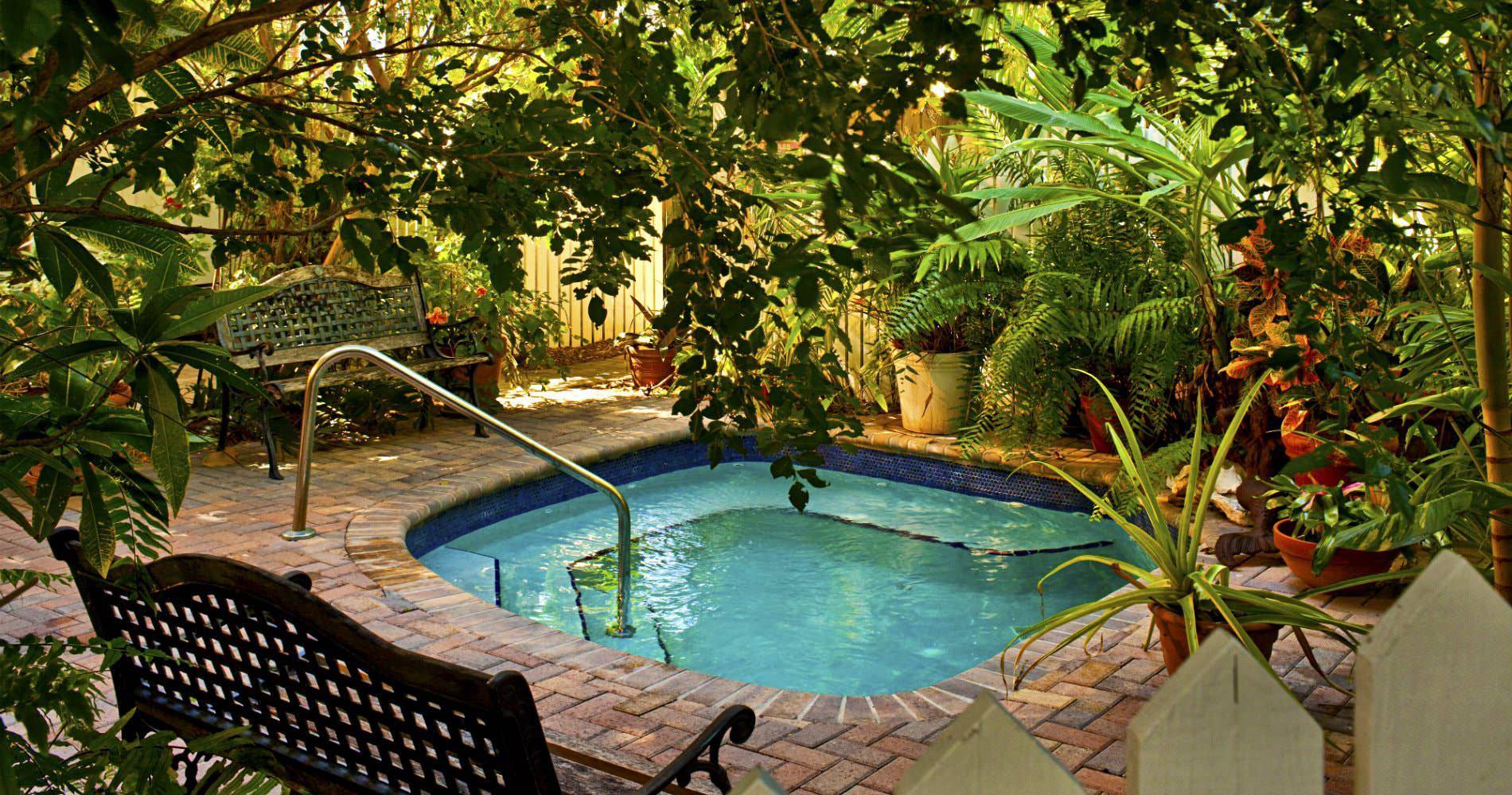 2 metal and wood benches with square pool surrounded by ferns and other plants all enclosed within picket fence